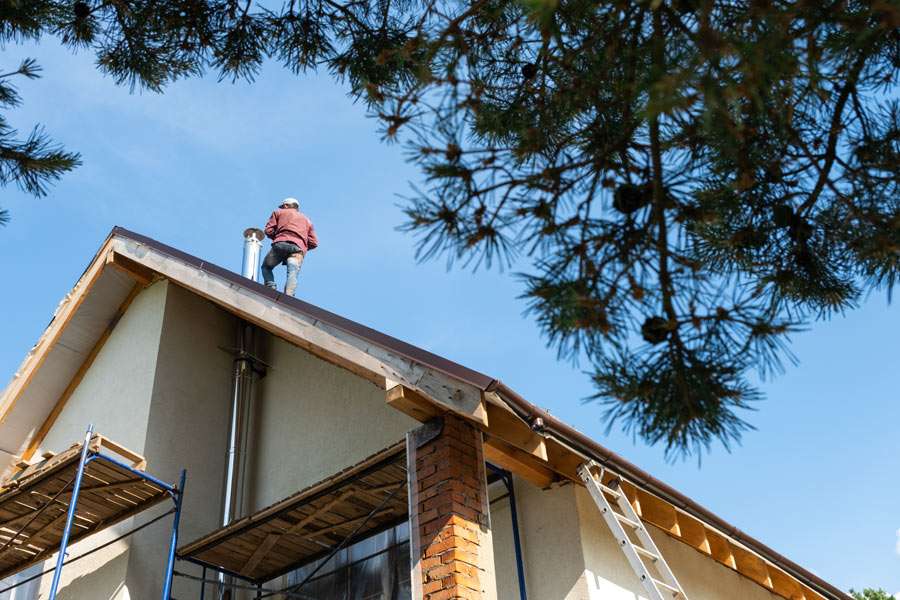 Person working on house roof with ladder and scaffolding.