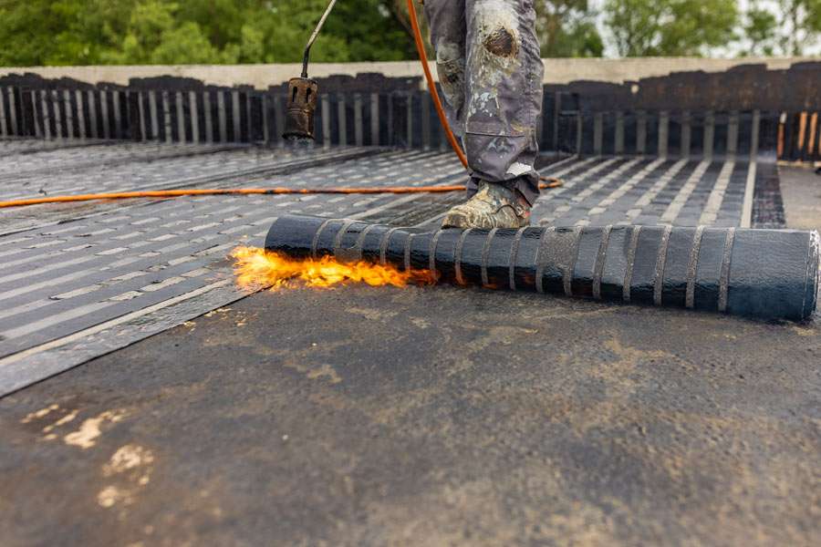 Worker torch-applying waterproof roofing material.
