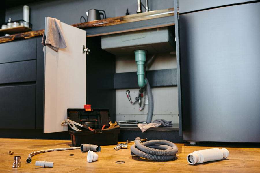 Kitchen sink plumbing repair with tools and parts.