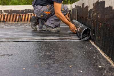 Worker installing waterproofing on foundation.